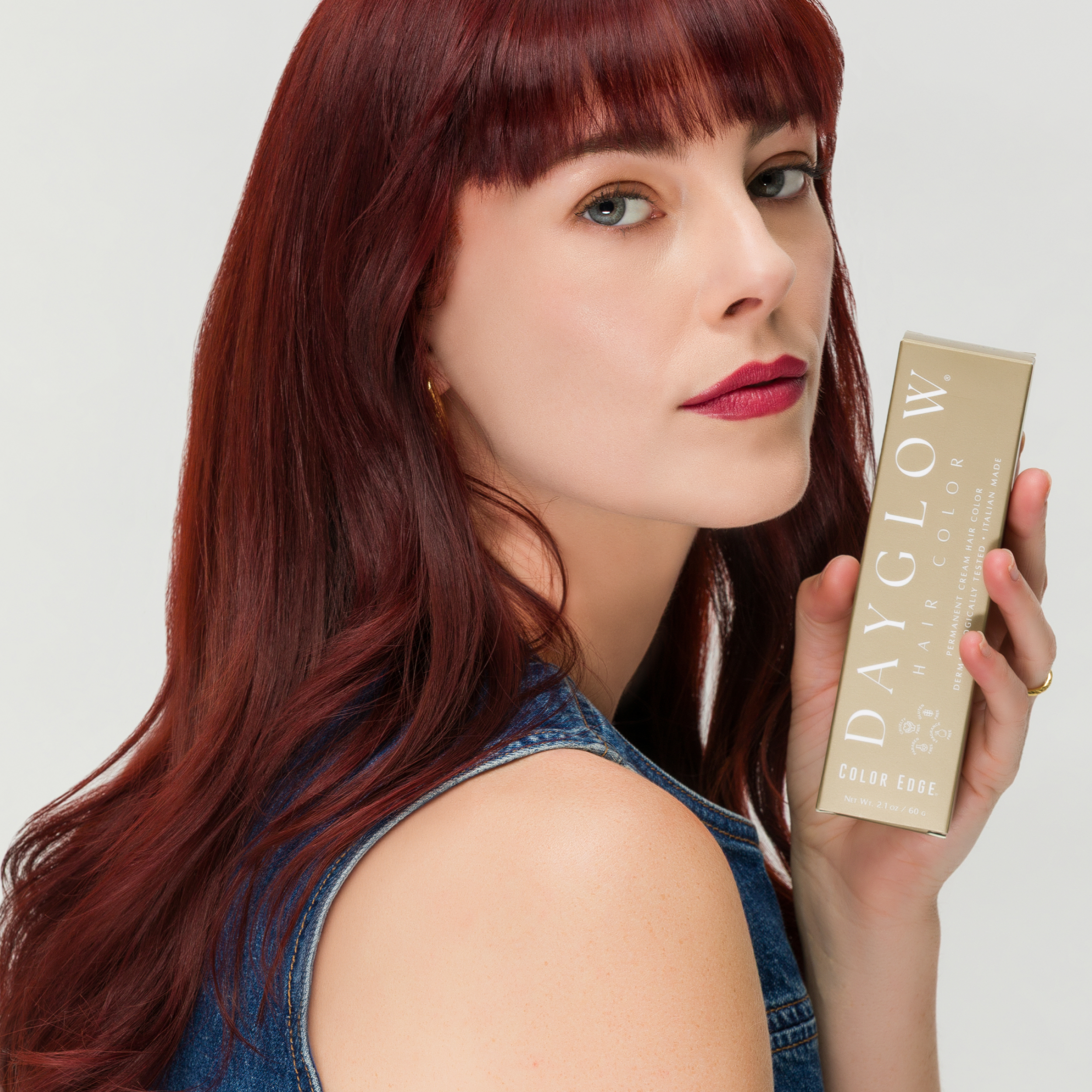Model with cherry red hair holding up a box of Dayglow Hair Color